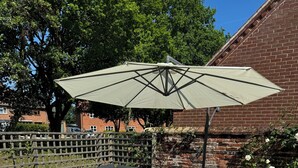 Une terrasse extérieure avec un ensemble de meubles de jardin en osier gris, une table avec des verres à vin et un grand parasol.