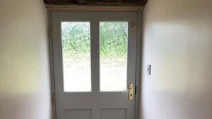 Une porte fermée avec une fenêtre, une poignée de porte et un interrupteur sur le mur.