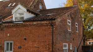 Un bâtiment en briques avec un toit à deux versants, une petite lucarne et une porte sur laquelle est fixée une enseigne.
