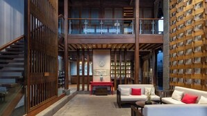 A spacious lobby with a high ceiling, a staircase, a seating area with a sofa and armchairs, and a large wooden wall. - Huayu Donglin Boutique Holiday Hotel (Lijiang)