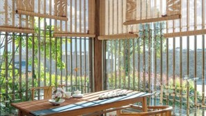 A dining area with a wooden table, chairs, and a view through bamboo screens to a garden and water. - Huayu Donglin Boutique Holiday Hotel (Lijiang)