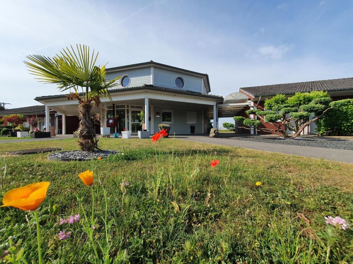 A two-story building with a covered porch, a palm tree, and a garden with flowers.