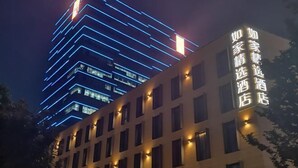A hotel building with illuminated signage in a foreign language, adjacent to a taller building with blue lighting. - Homeinn Plus Hotel (Suzhou Fenhu Luxin Avenue) (Suzhou)