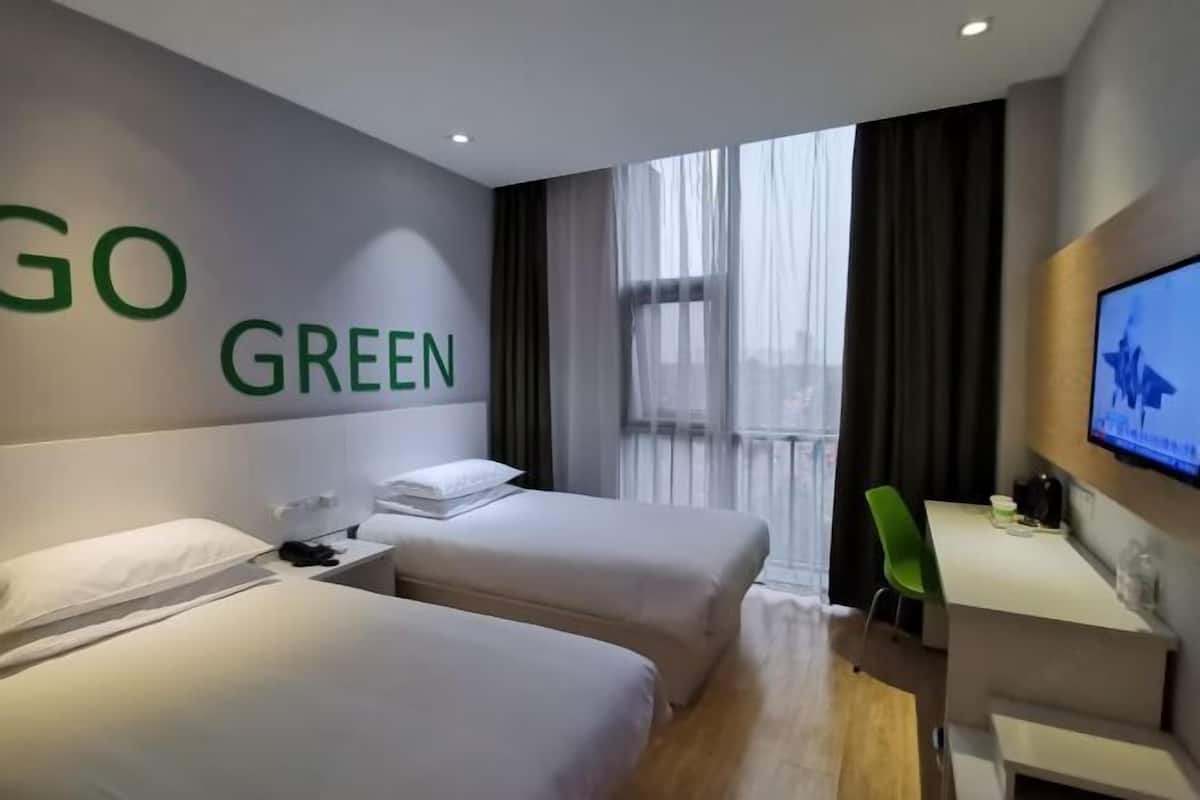 Habitación de hotel con dos camas, un escritorio, una silla y un televisor en la pared.