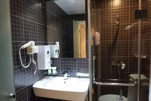 Ein Badezimmer mit weißem Waschbecken, dunklen Fliesenwänden, einer Duschkabine aus Glas und einem Spiegel.