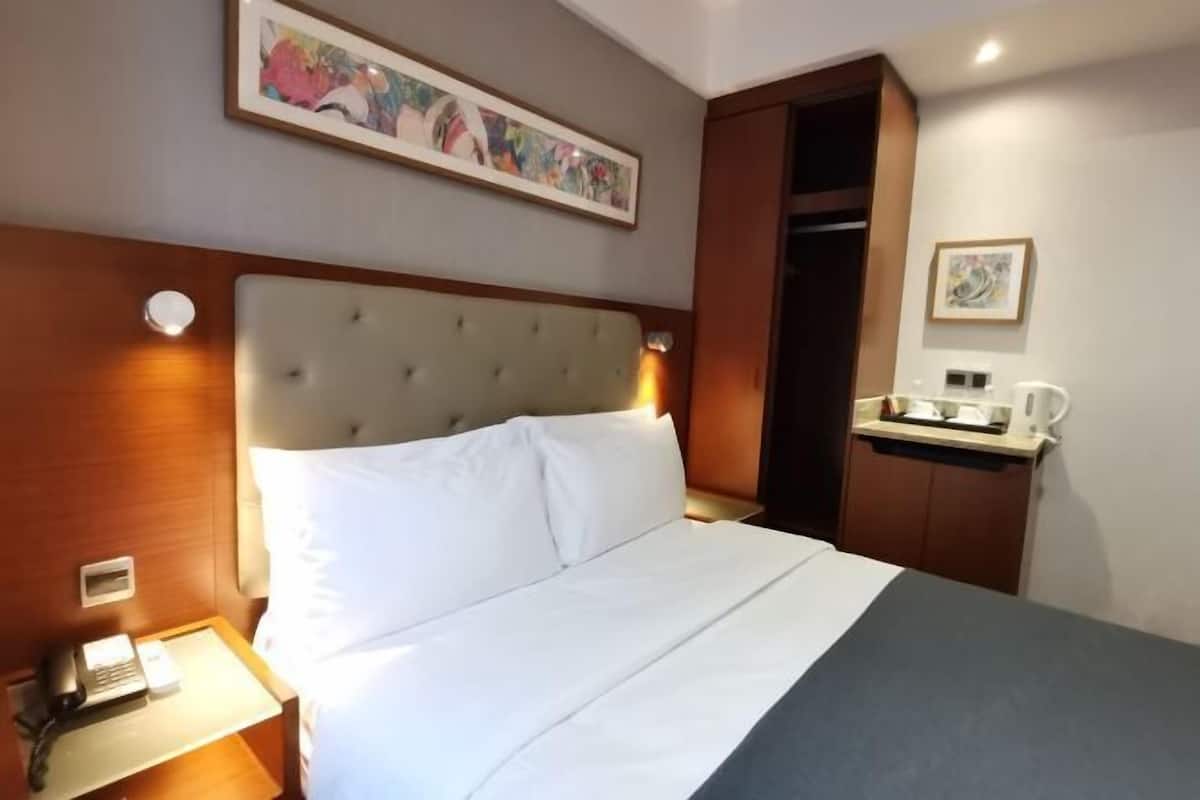 Una habitación de hotel con una cama grande, una mesita de noche con teléfono, una pequeña mesa con cafetera y una puerta que da a un armario.