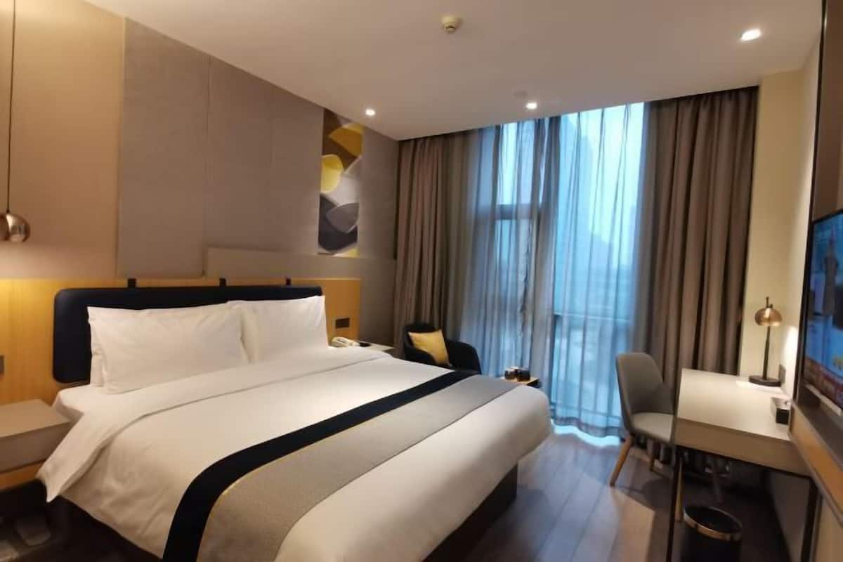 Una habitación de hotel con una cama grande, un escritorio, una silla y un ventanal con cortinas.