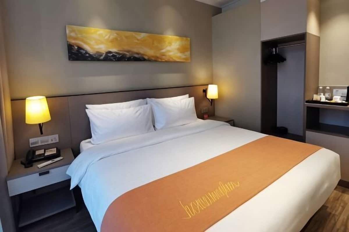 Una habitación de hotel con una cama, mesitas de noche, un cuadro y una estantería con objetos.