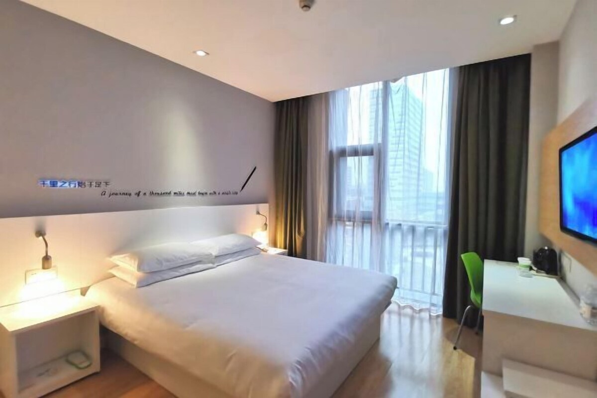Ein Hotelzimmer mit Bett, Nachttisch, Fernseher und einem Fenster mit Vorhängen.