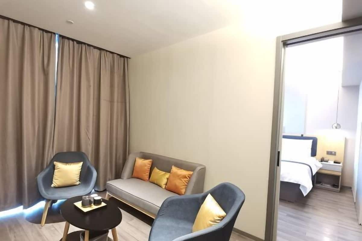 Una habitación de hotel moderna con sofá, dos sillones, una mesita y una cama.