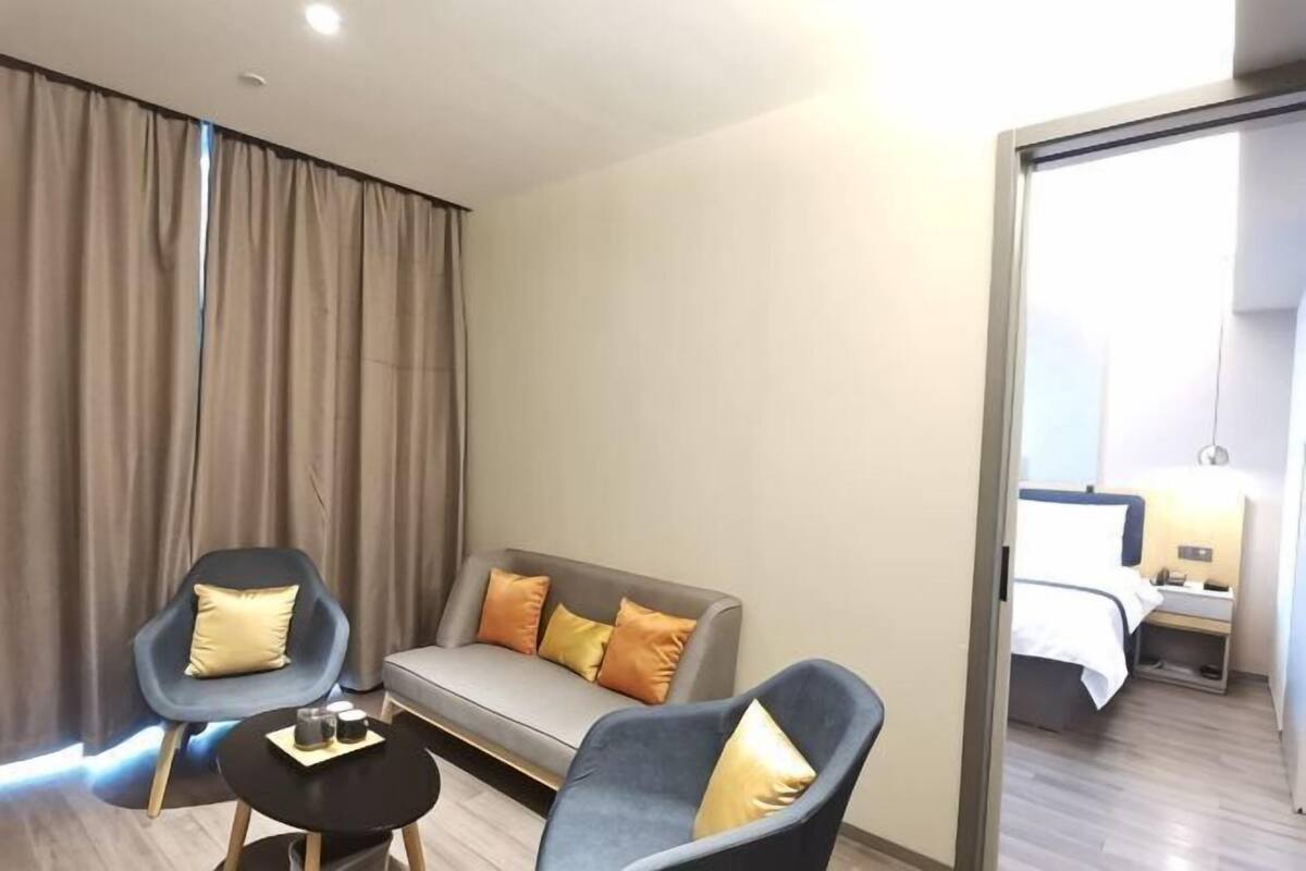 A modern hotel room with a sofa, two armchairs, a small table, and a bed.
