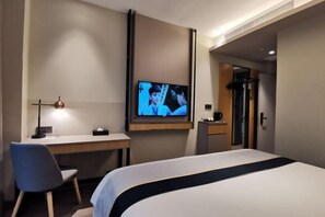 Ein Hotelzimmer mit einem Bett, einem Schreibtisch, einem Stuhl, einem an der Wand befestigten Fernseher und einer Tür zu einem weiteren Raum.