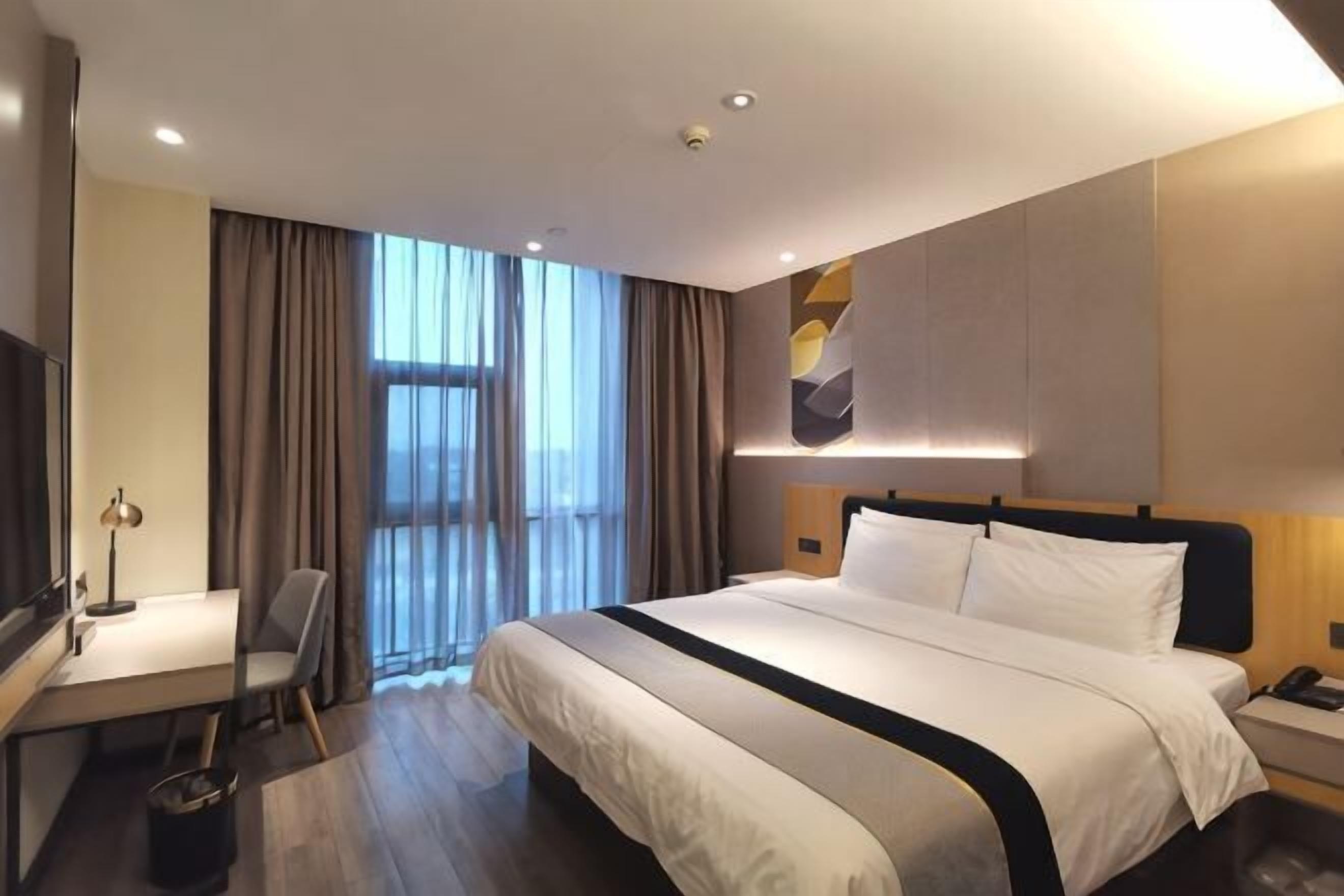 Habitació d'hotel amb un llit gran, una escriptori amb una cadira, una televisió i una finestra amb cortines.