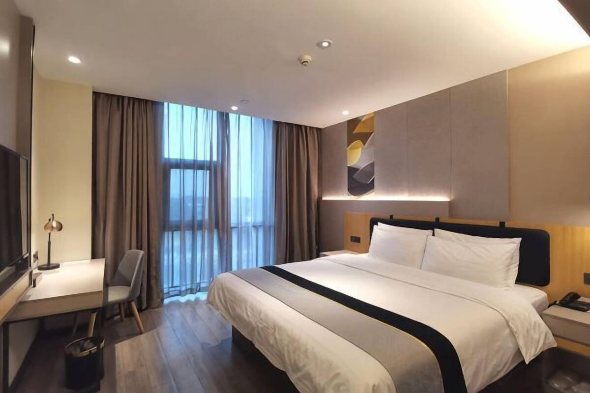Habitación de hotel con una cama grande, un escritorio con silla, televisión y una ventana con cortinas.