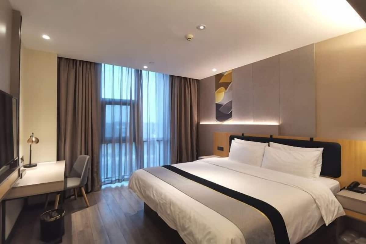 A hotel room with a large bed, a desk with a chair, a TV, and a window with curtains.