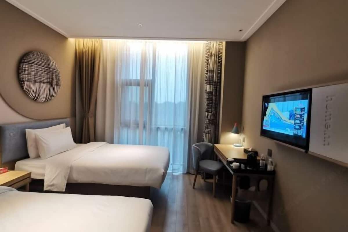Habitación de hotel con dos camas, un escritorio con lámpara, televisión y vistas al exterior.