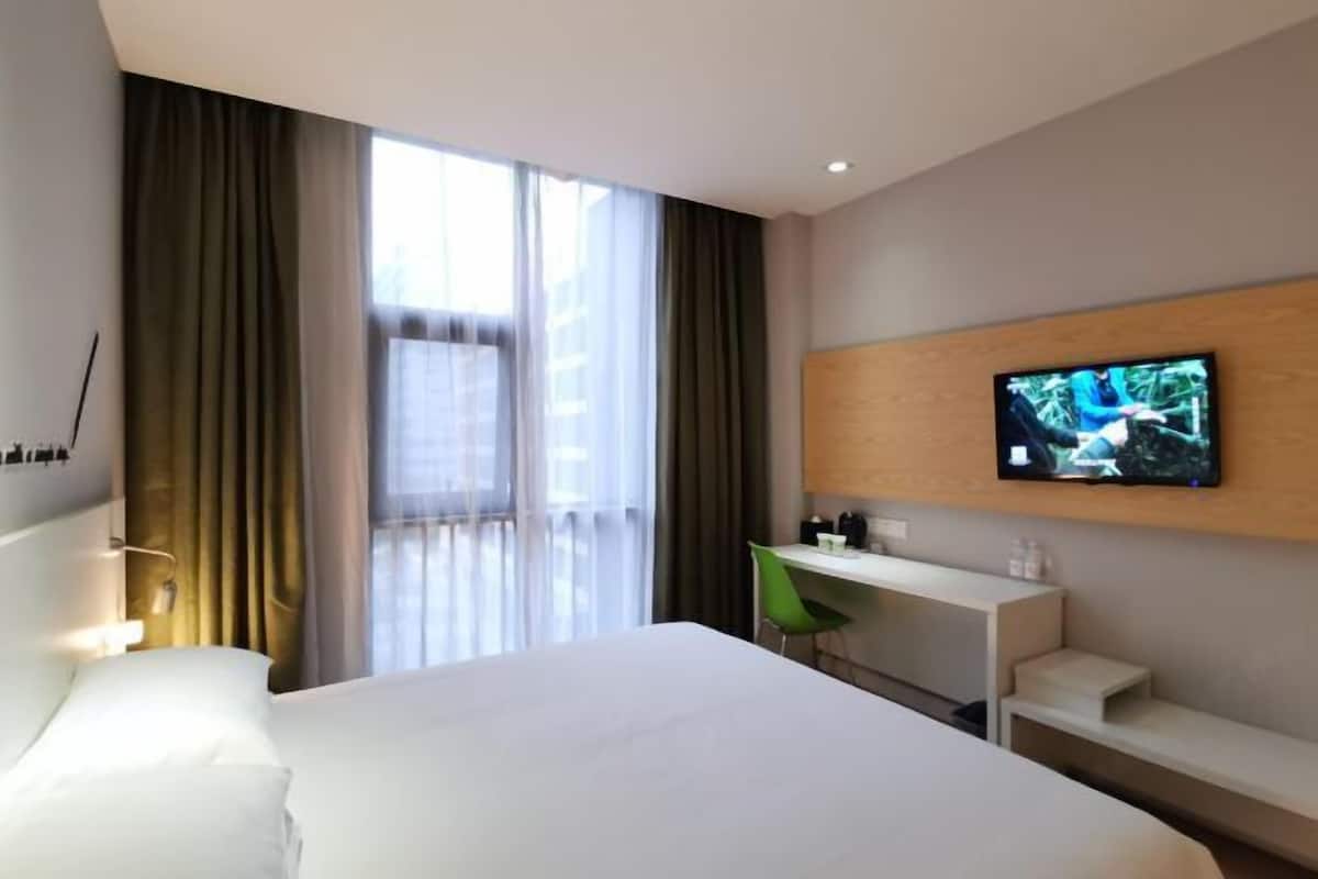 Una habitación de hotel con cama, escritorio, silla, televisor y ventana con cortinas.