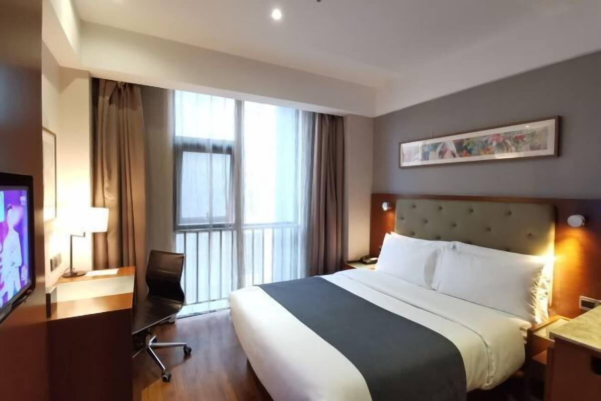 Habitación de hotel con cama, escritorio, silla, televisor y ventana con cortinas.