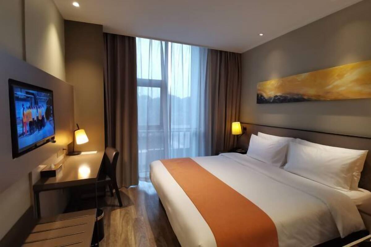 Una habitación de hotel con cama, escritorio, televisor y un cuadro en la pared.