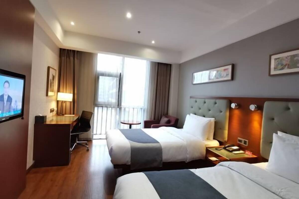 Habitación de hotel con dos camas, un escritorio, un televisor y un balcón.