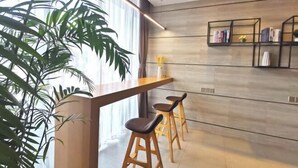A modern kitchen with a wooden countertop, two bar stools, a bookshelf, and a large window with plants. - Homeinn Plus Hotel (Suzhou Fenhu Luxin Avenue) (Suzhou)