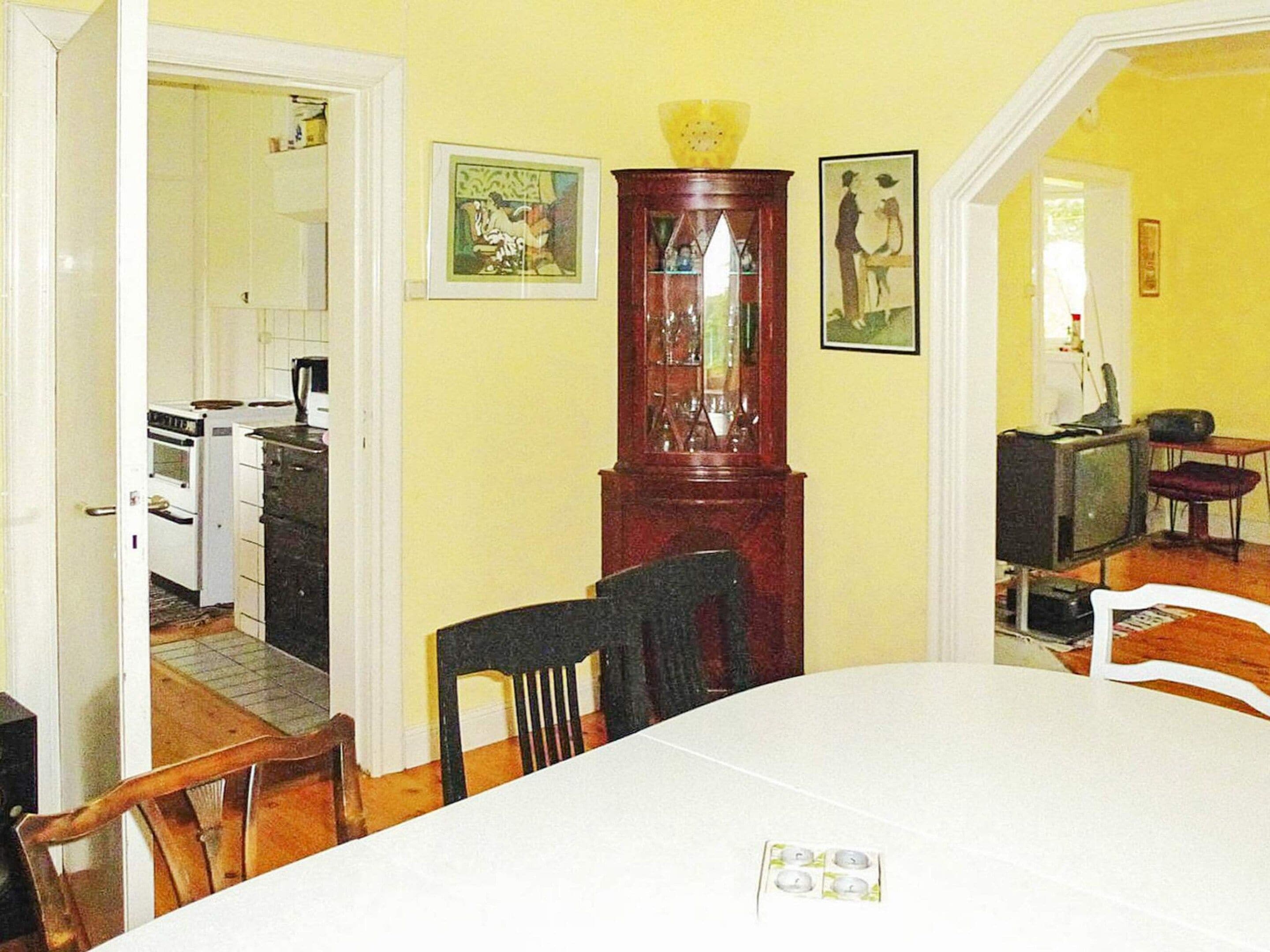Un comedor con una mesa, sillas, un armario de madera y una cocina al fondo.