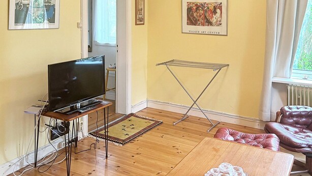 A living room with a television on a stand, a drying rack, a sofa, and a window with curtains.
