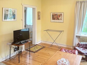 A living room with a television on a stand, a drying rack, a sofa, and a window with curtains.