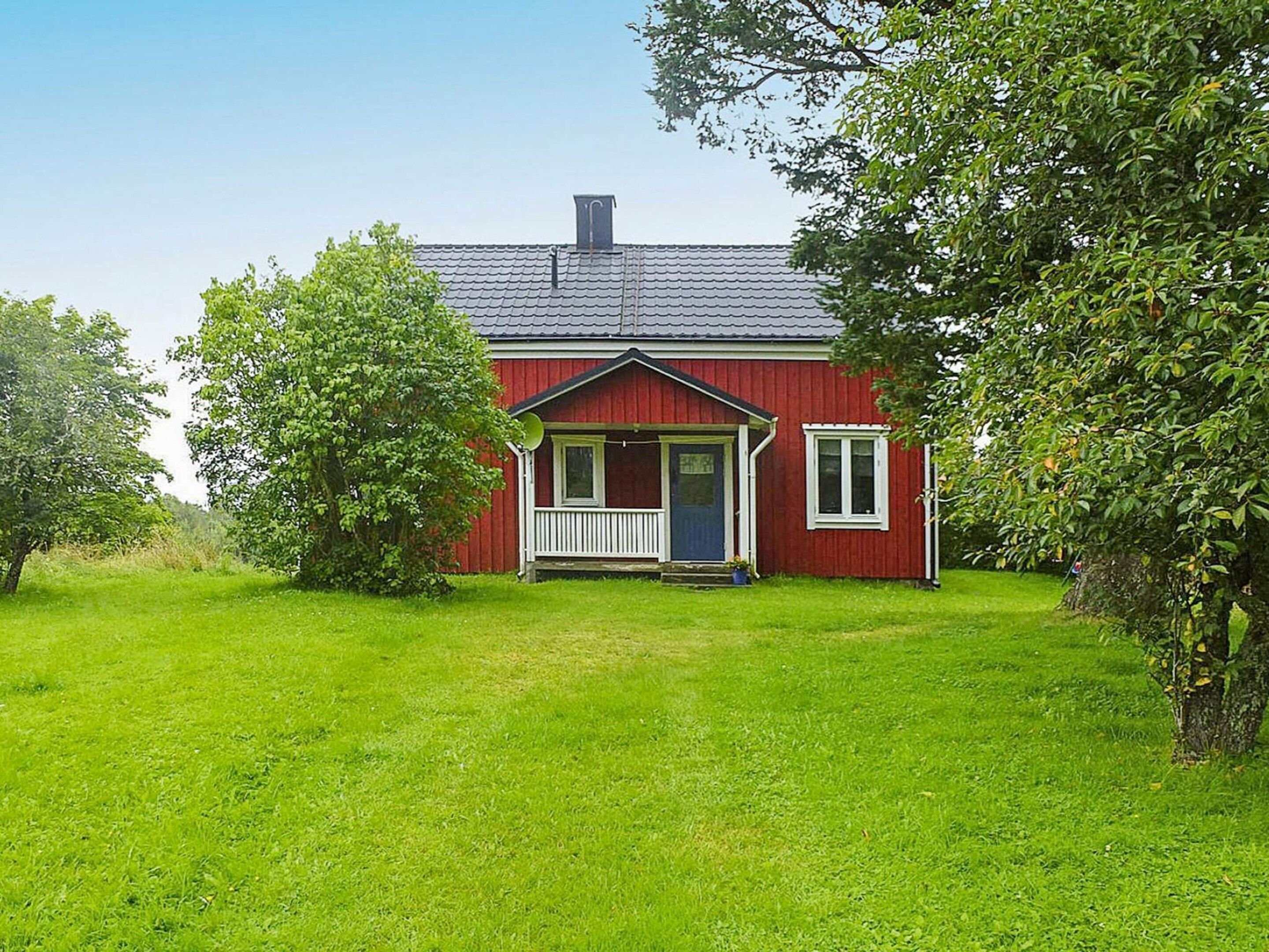 A red house with a porch, surrounded by green grass and trees.