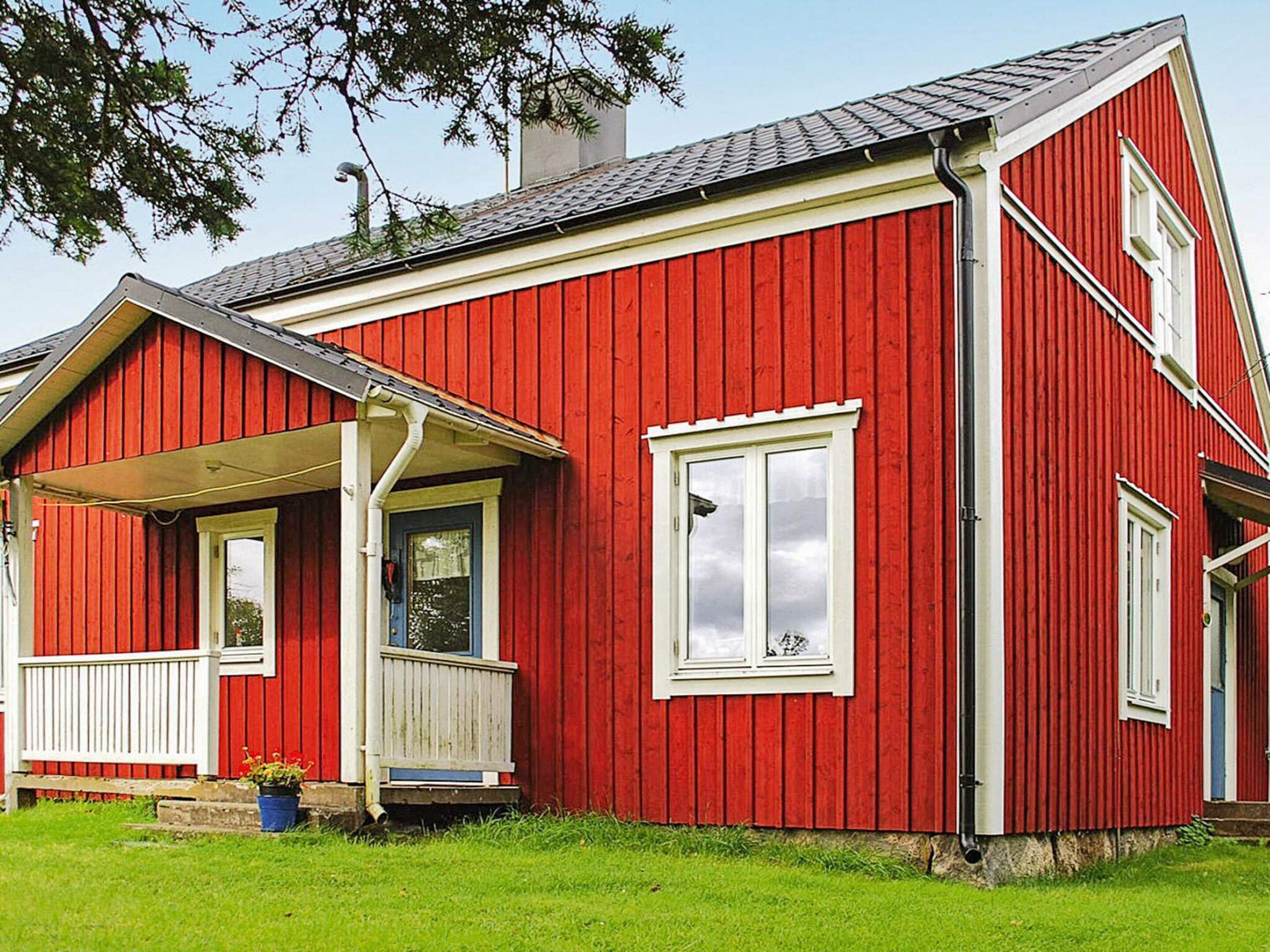 A red wooden house with a porch, a chimney, and a window.