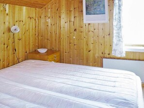 Une pièce comprenant un lit, une commode en bois, une lampe fixée au mur et une fenêtre avec un rideau.