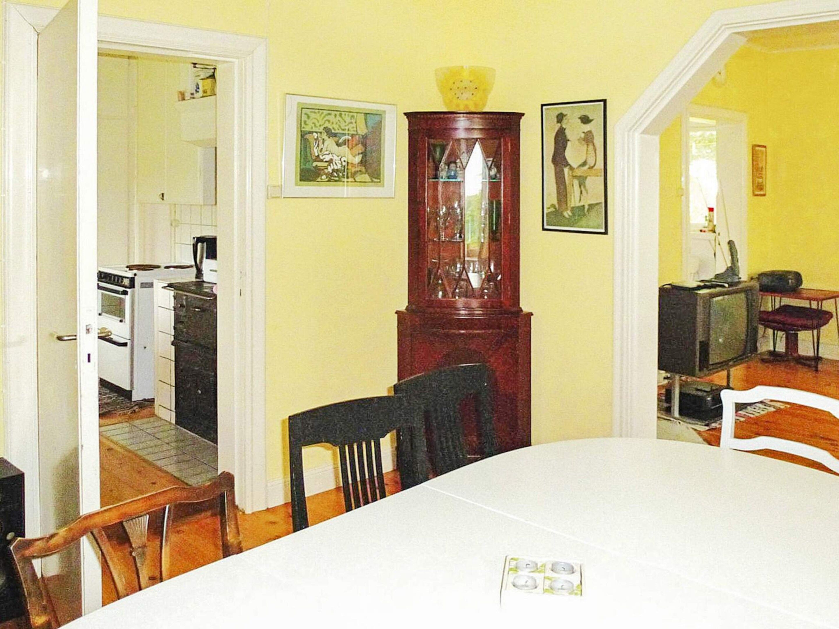 A dining area with a white table and chairs, a wooden cabinet, and a television in the background.