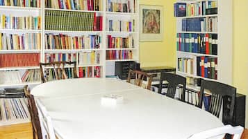Um quarto com uma mesa branca rodeada por cadeiras, uma estante cheia de livros e um quadro emoldurado na parede.