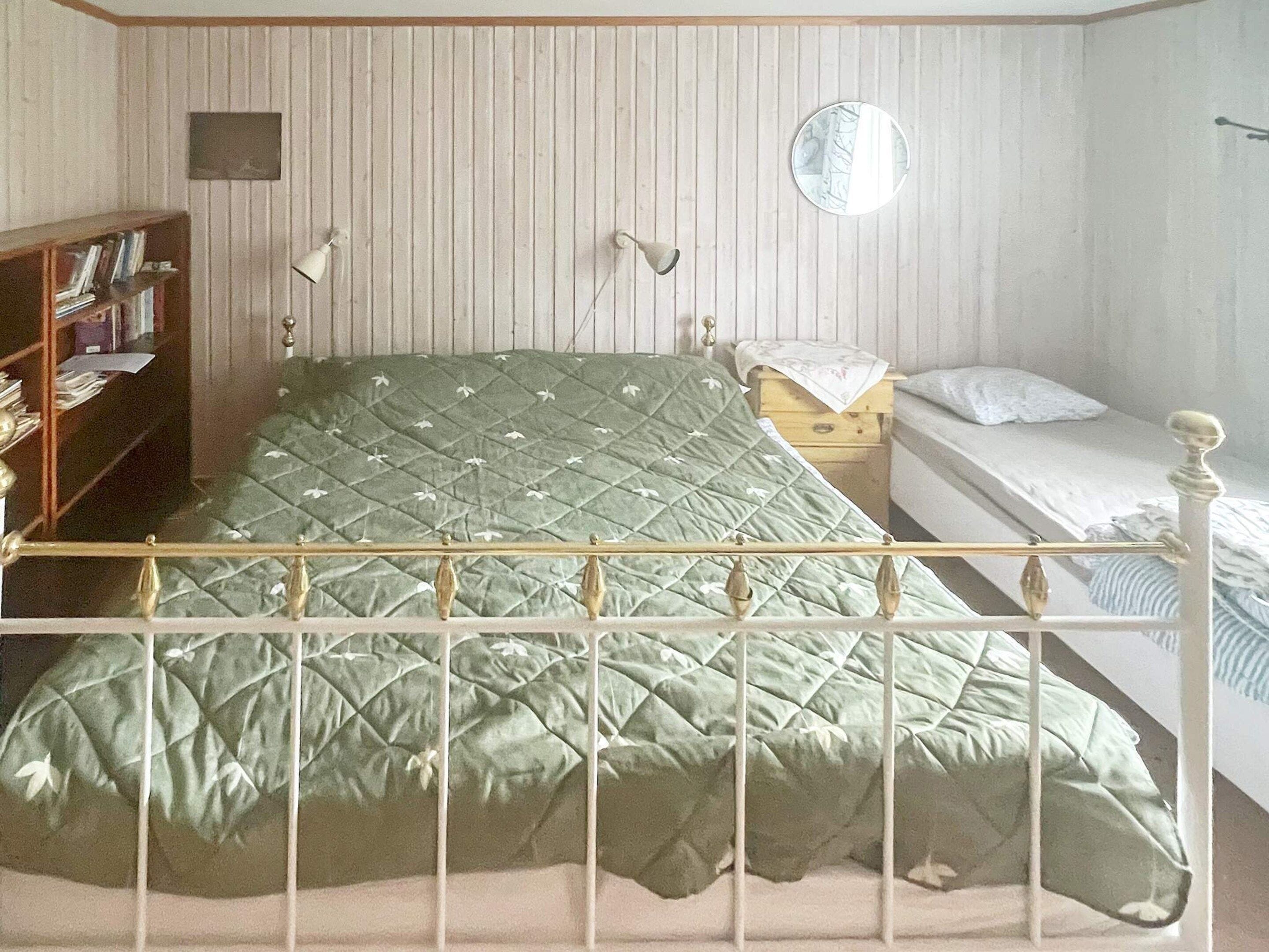 Una habitación con una cama, una mesita de noche, una lámpara, un espejo y una estantería.