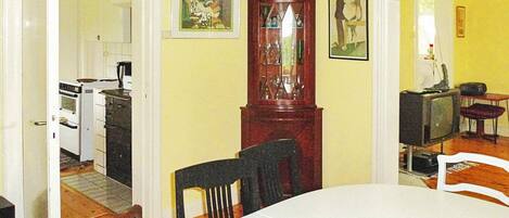 A dining area with a table, chairs, a wooden cabinet, and a kitchen in the background.