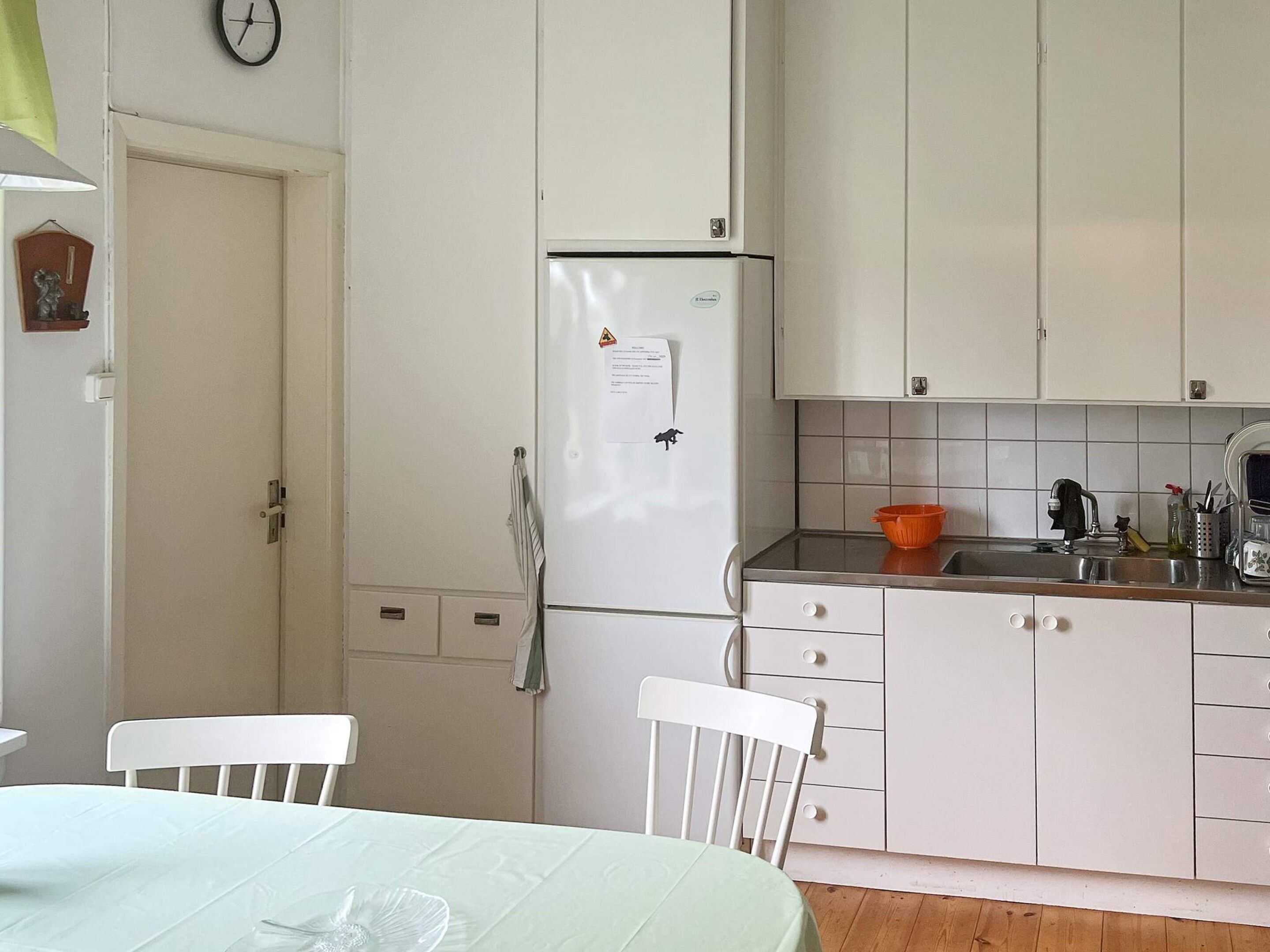 Una cocina con armarios blancos, un refrigerador, un lavabo y una mesa de comedor con sillas.