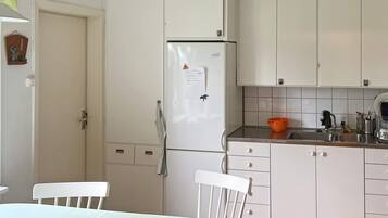 Una cocina con armarios blancos, un refrigerador, un lavabo y una mesa de comedor con sillas.