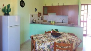 A compact kitchen with a refrigerator, a dining table with chairs, and a small island with a sink and cabinets. - Villa Selenia, completamente autonoma a pochi metri dal mare! (JOPPOLO)