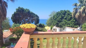 A balcony with a view of the sea, surrounded by lush greenery and a potted plant. - Villa Selenia, completamente autonoma a pochi metri dal mare! (JOPPOLO)