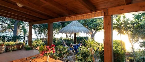 An outdoor wooden deck with a table, a thatched umbrella, and potted plants.