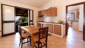 A compact kitchen with wooden cabinets, a dining table with chairs, and a view through an open door. - A corner of paradise waiting only for you! (JOPPOLO)