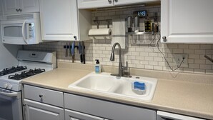 Une cuisine moderne avec des armoires blanches, un évier en acier inoxydable, un four à micro-ondes, une cuisinière et une horloge numérique affichant 1 h 49.