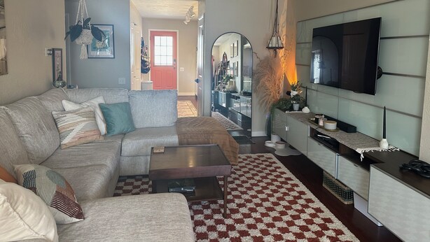 Un salon moderne avec un canapé d’angle, une table basse, un téléviseur fixé au mur et un tapis à motifs.