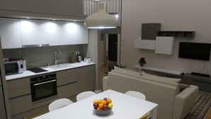A modern kitchen with a dining area, white furniture, and a flat-screen TV mounted on the wall. - Opera Suites - Aida (Palermo)