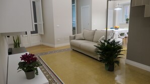 A modern living room with a sofa, a dining table with chairs, and potted plants. - Opera Suites - Aida (Palermo)