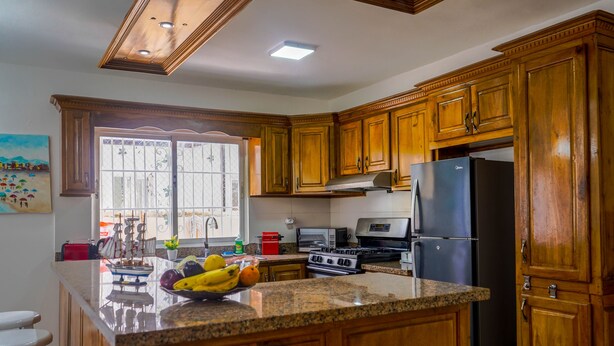 A kitchen with wooden cabinets, granite countertops, a refrigerator, stove, microwave, and a window with a view of the outdoors. - Beautiful 2-bed Villa in Punta Cana Bavaro (Punta Cana)