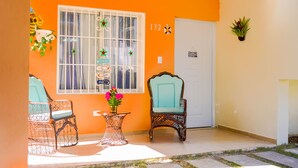 A room with a large window, two wicker chairs, a small table with a vase of flowers, and a door with a sign. - Beautiful 2-bed Villa in Punta Cana Bavaro (Punta Cana)