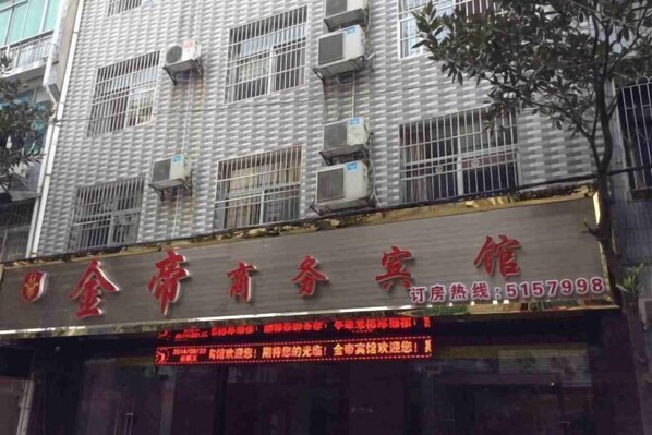 Fachada de hotel con múltiples unidades de aire acondicionado, un letrero rojo con caracteres chinos y un panel de señalización digital con texto rojo.