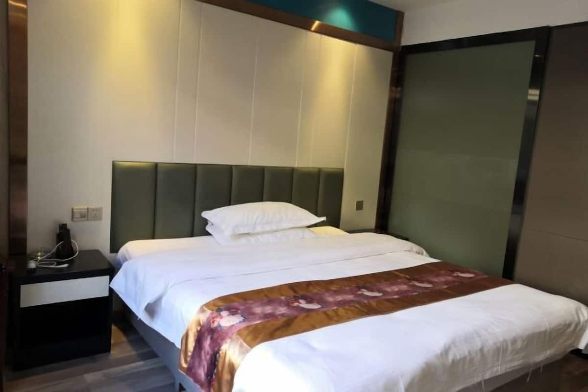 A hotel room with a bed, a nightstand, and a wall-mounted panel.