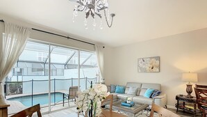 A spacious living area with a pool view, a dining table with chairs, and a sofa with decorative pillows.